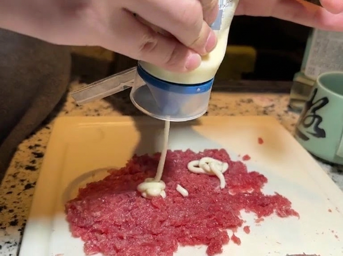 Spremuta di maionese bianca da una bottiglia su una porzione separata di tonno rosso crudo tritato.