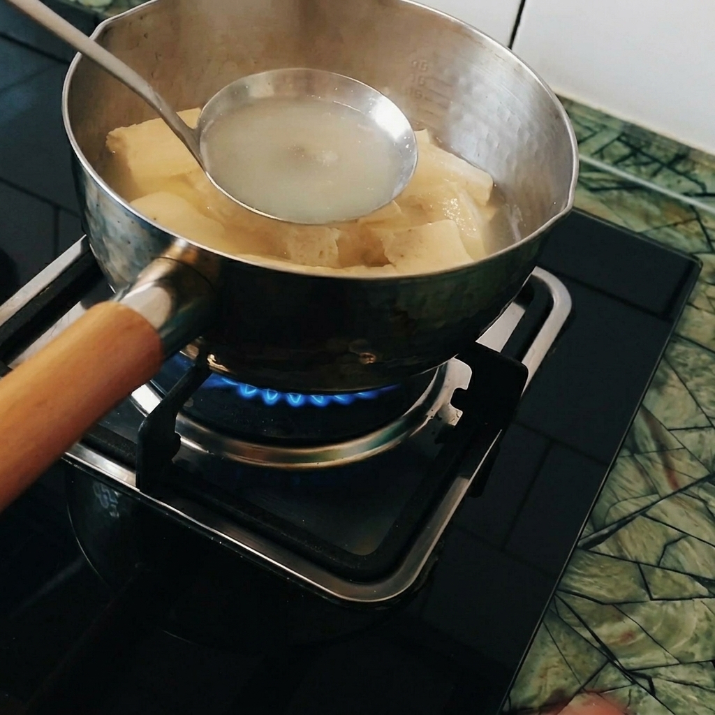 Pezzi di curry sciolti in un mestolo tenuto dentro la pentola di acqua bollente.