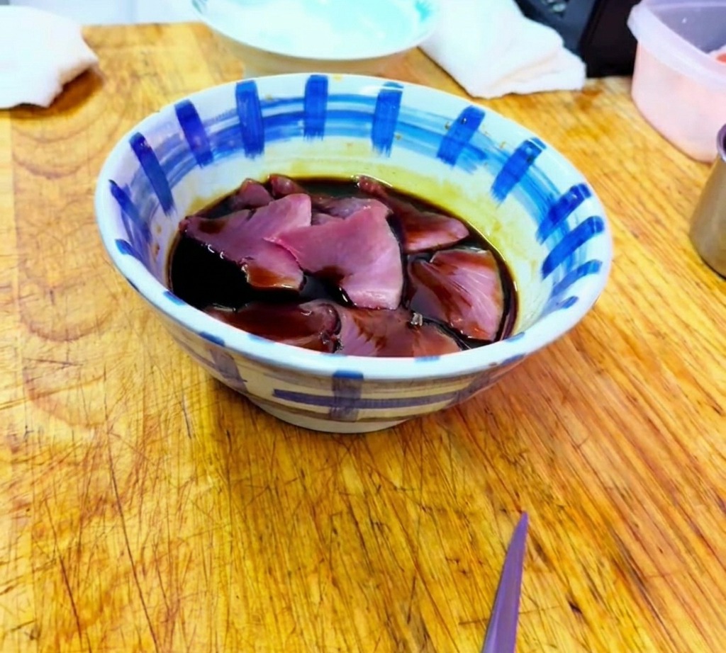 Fette di tonno crudo immerse in una marinata scura e saporita a base di soia allinterno di una ciotola di ceramica decorata.