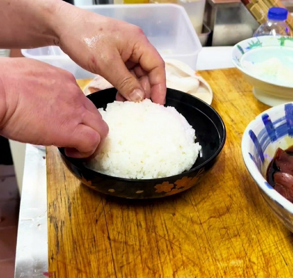 Riso bianco cotto che viene delicatamente modellato e livellato allinterno di una ciotola da portata nera.