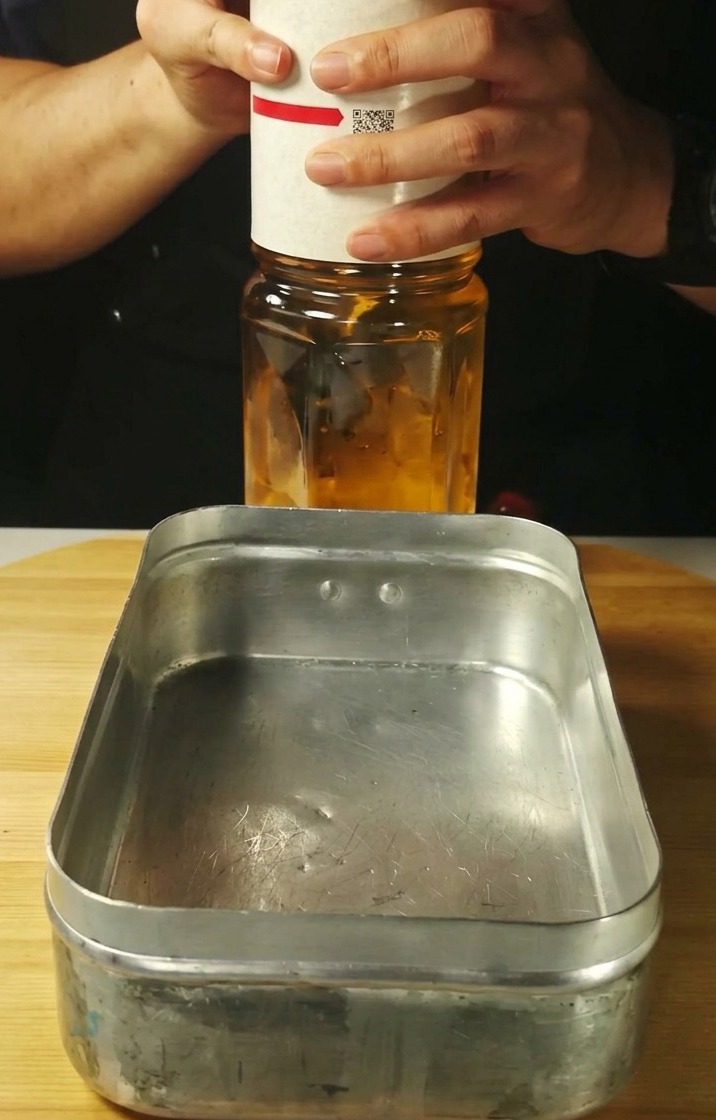 Liquido trasparente versato in un vassoio di metallo rettangolare.