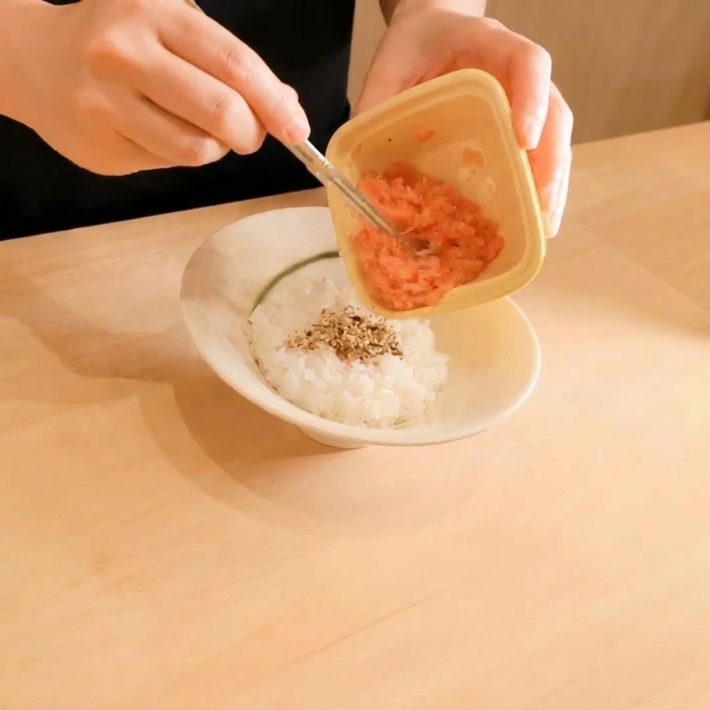 Tonno crudo tritato prelevato da un piccolo contenitore di plastica e adagiato su un letto di riso bianco cosparso di semi di sesamo.
