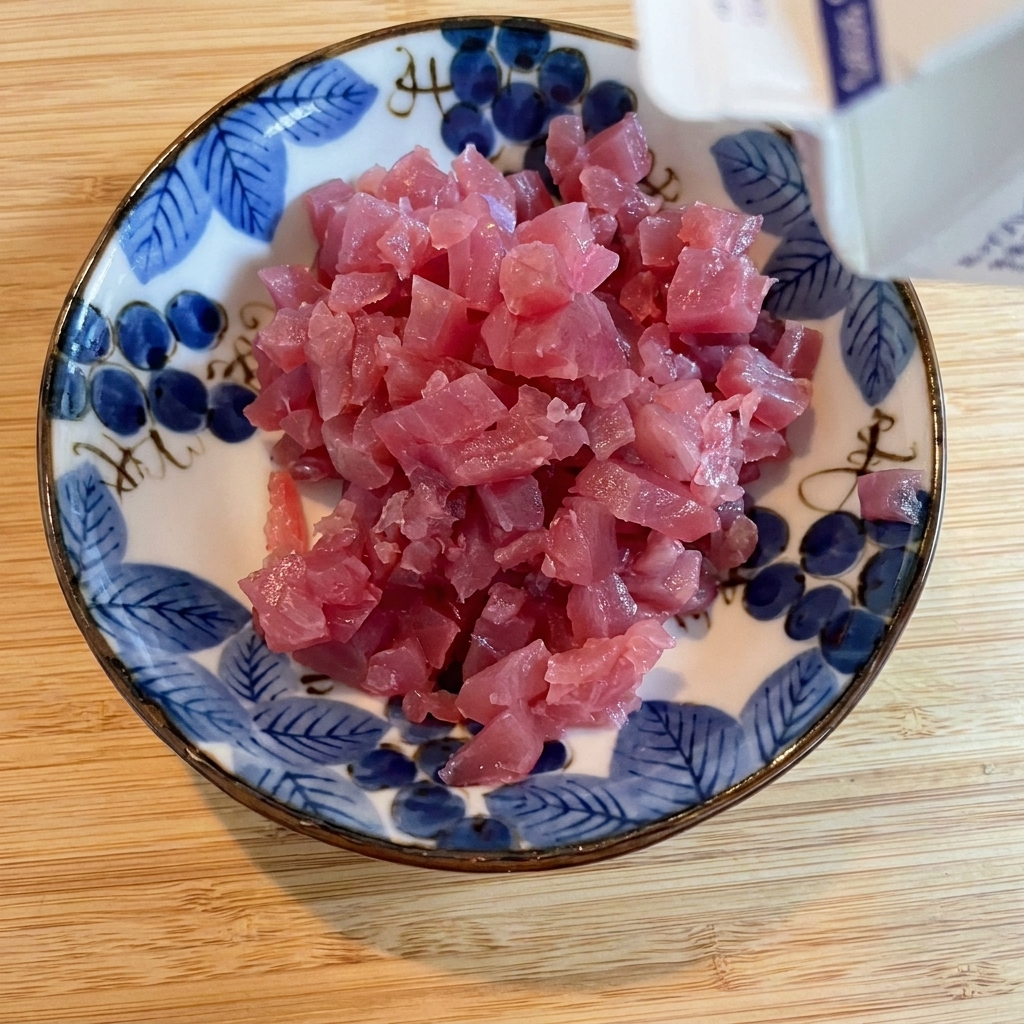 Salsa di soia versata a filo sui cubetti di tonno in una ciotola decorata.
