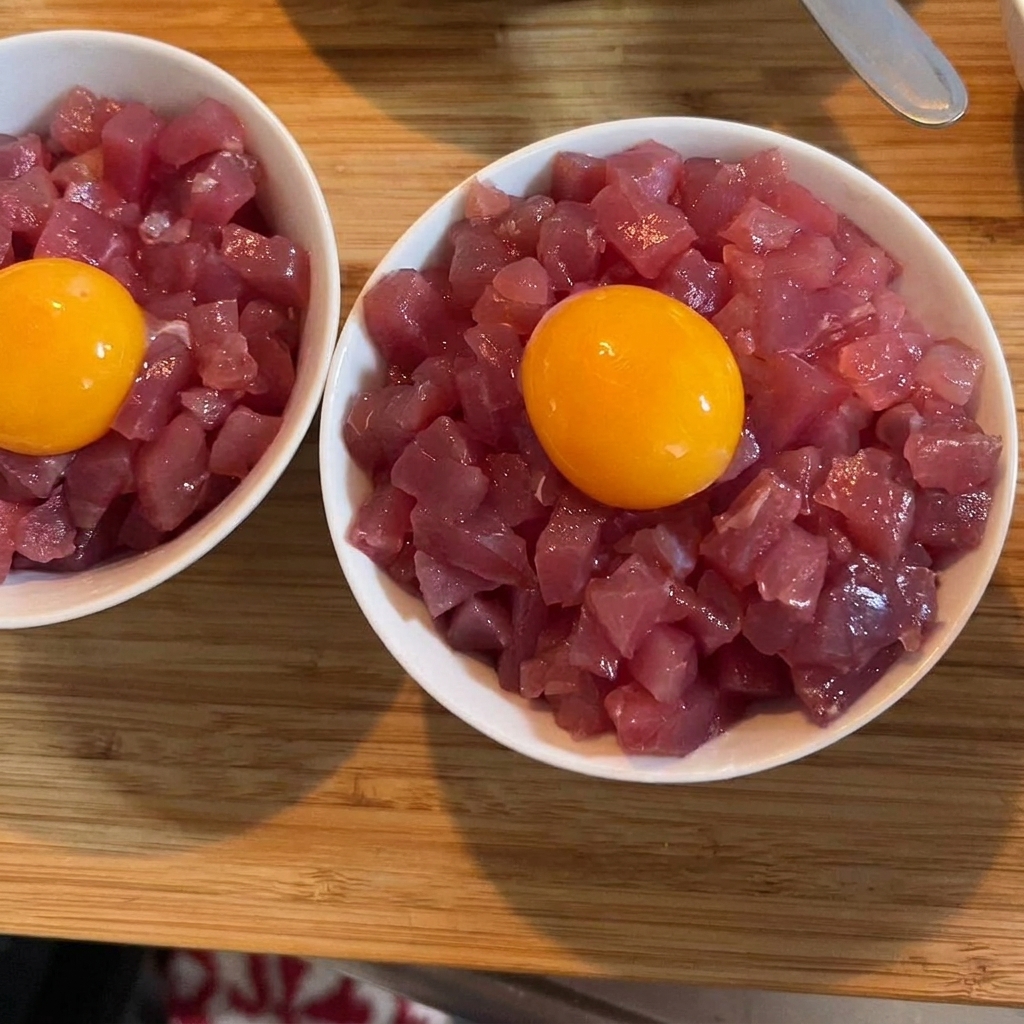 Un vivace tuorlo duovo crudo dorato appoggiato sopra una ciotola di tonno e riso, guarnito con cipollotto verde.