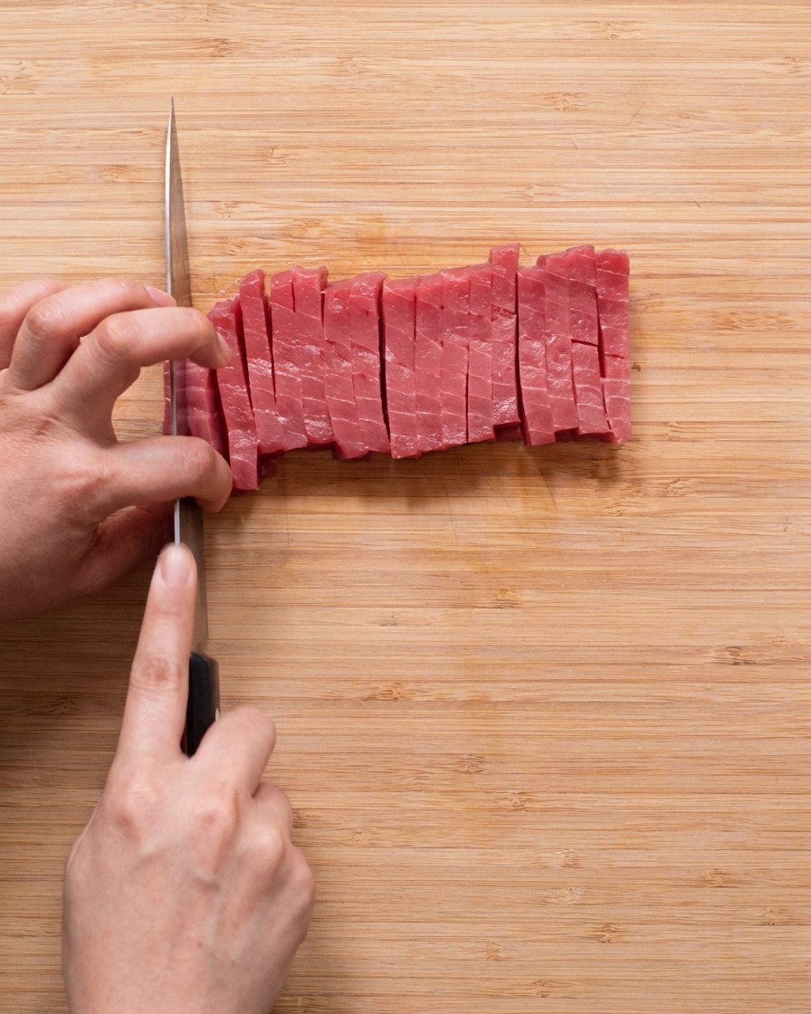 Cubetti uniformi di tonno rosso crudo disposti su un tagliere di legno.