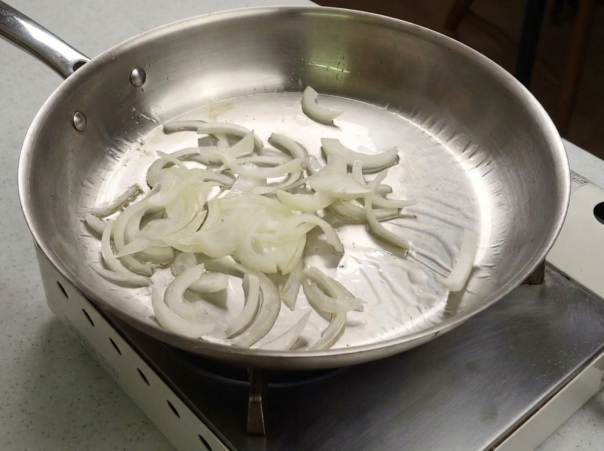 Strisce di cipolla bianca saltate in una padella in acciaio inossidabile.