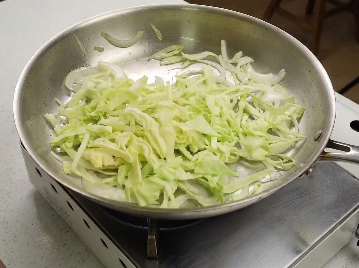 Cavolo verza affettato sottilmente aggiunto in padella con cipolle saltate.