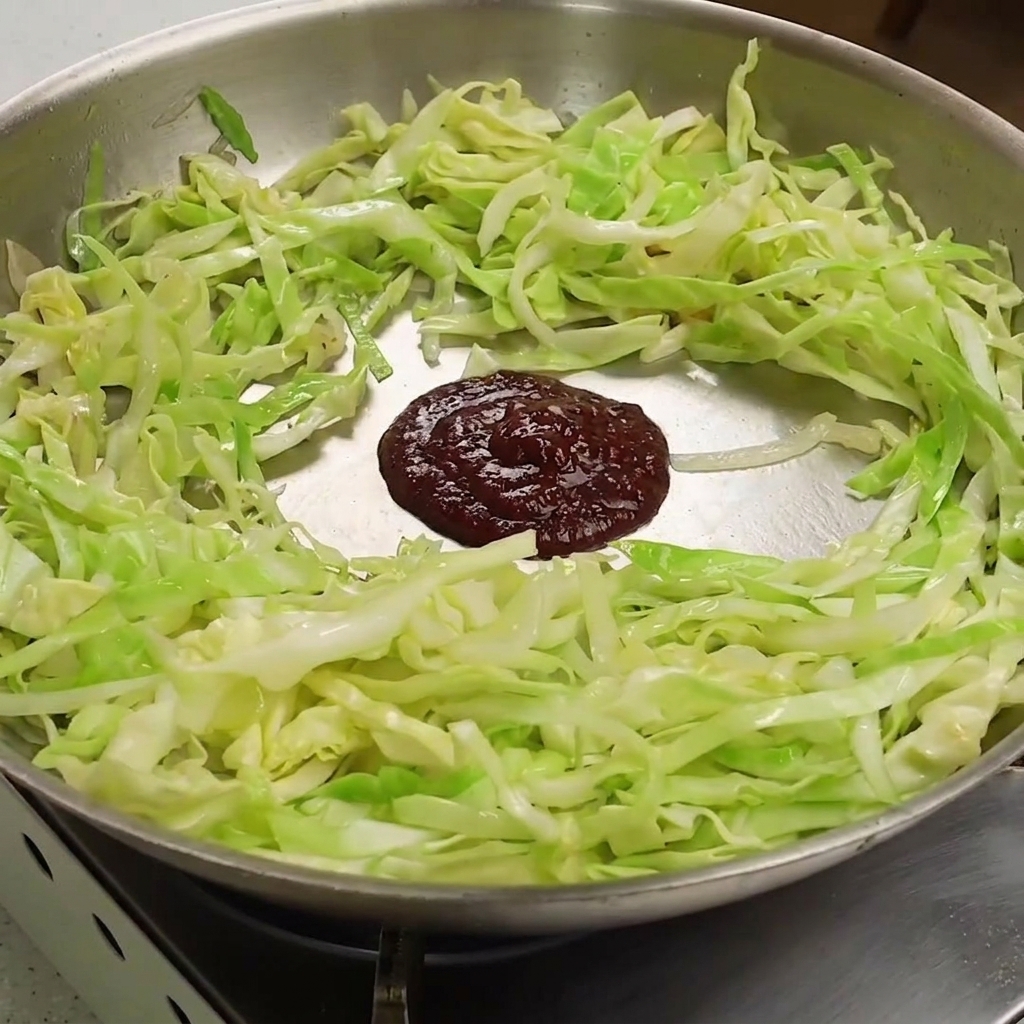 Una goccia di pasta di peperoncino e soia scura sopra il cavolo ammorbidito in padella.