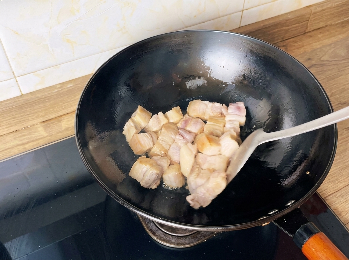 Cubetti di pancia di maiale saltati in un wok con una spatola fino a doratura.