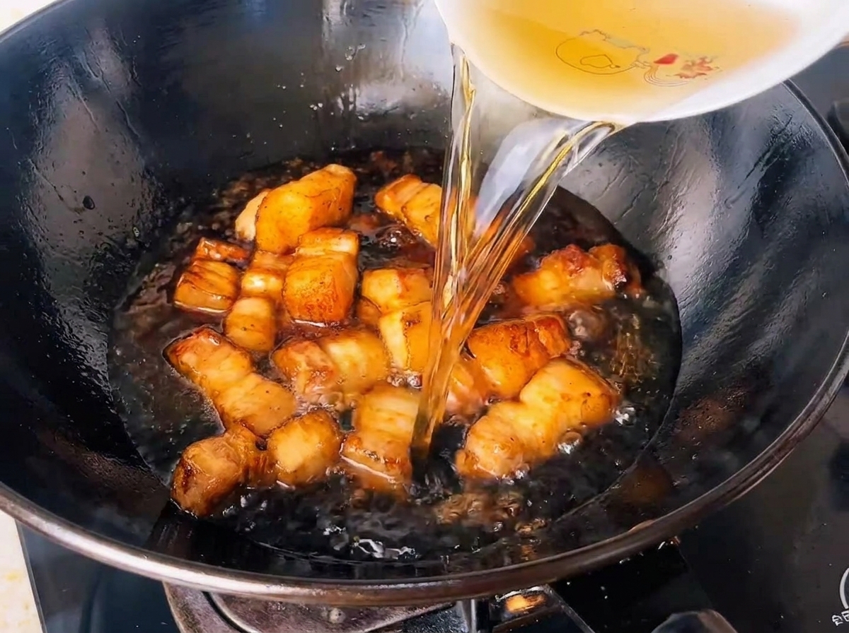 Acqua di tè verde infusa versata in un wok pieno di cubetti di maiale conditi.