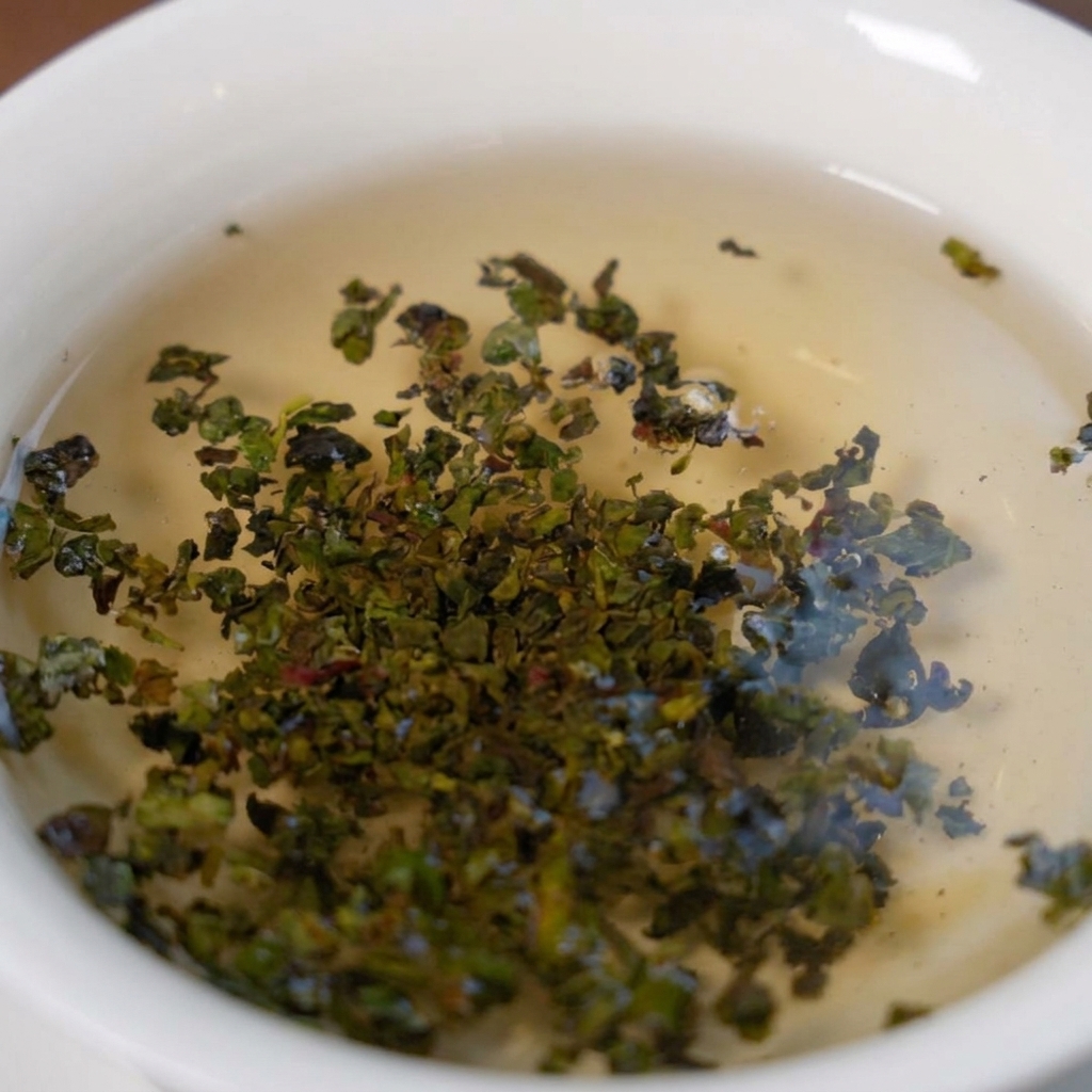 Foglie verdi di tè Tieguanyin che si espandono in infusione in una ciotola bianca piena di acqua calda.