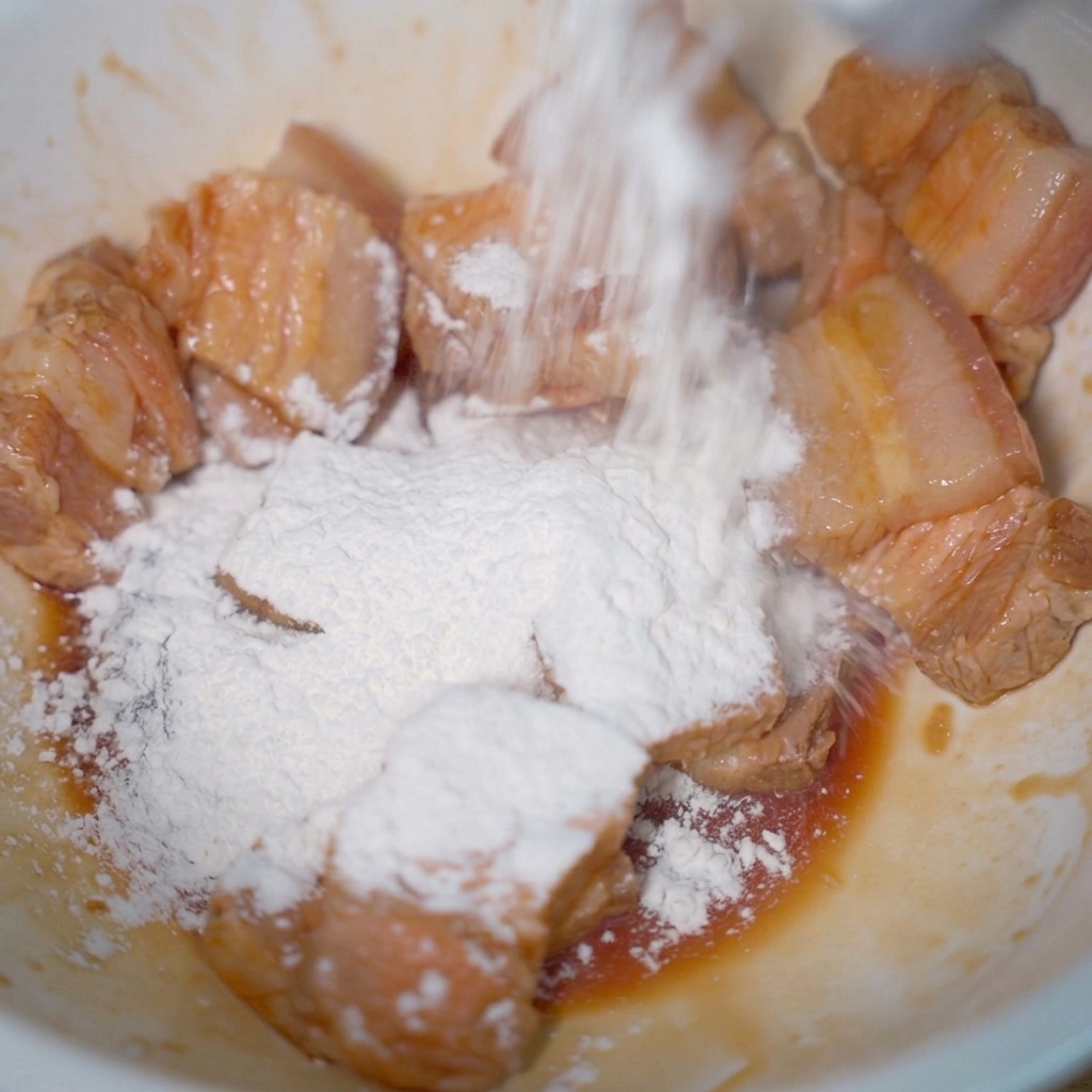 Fette chiare di maiale in una ciotola coperte da uno spesso strato di amido di tapioca bianco.