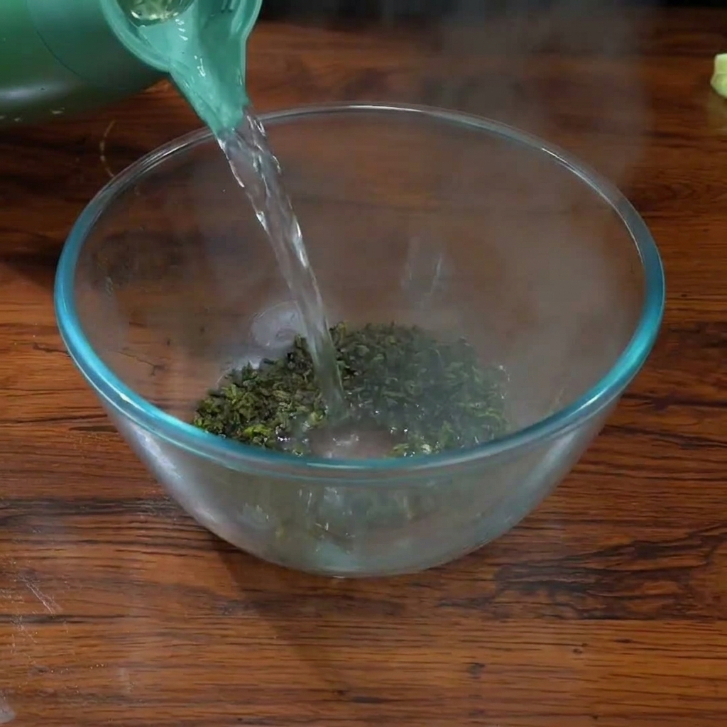 Versare acqua bollente da un bollitore verde sulle foglie di tè Tieguanyin in una ciotola di vetro trasparente.