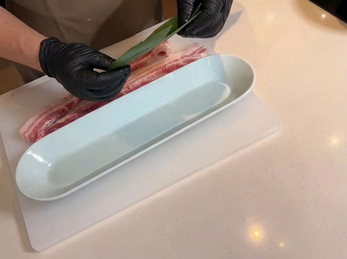 Mani che posizionano una foglia di bambù su un vassoio bianco lungo accanto alla carne.