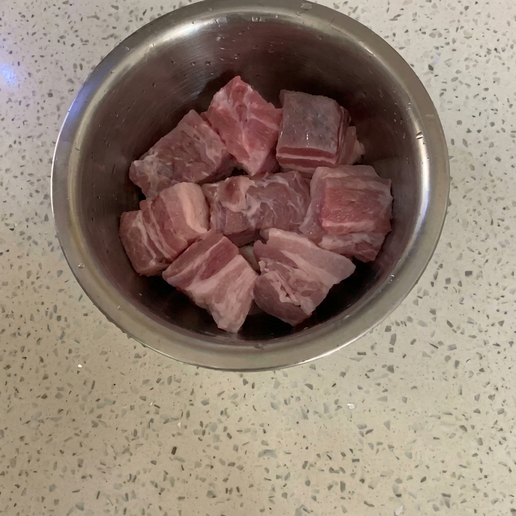 Cubetti di pancetta di maiale cruda in una ciotola di acciaio inox su un piano di lavoro.