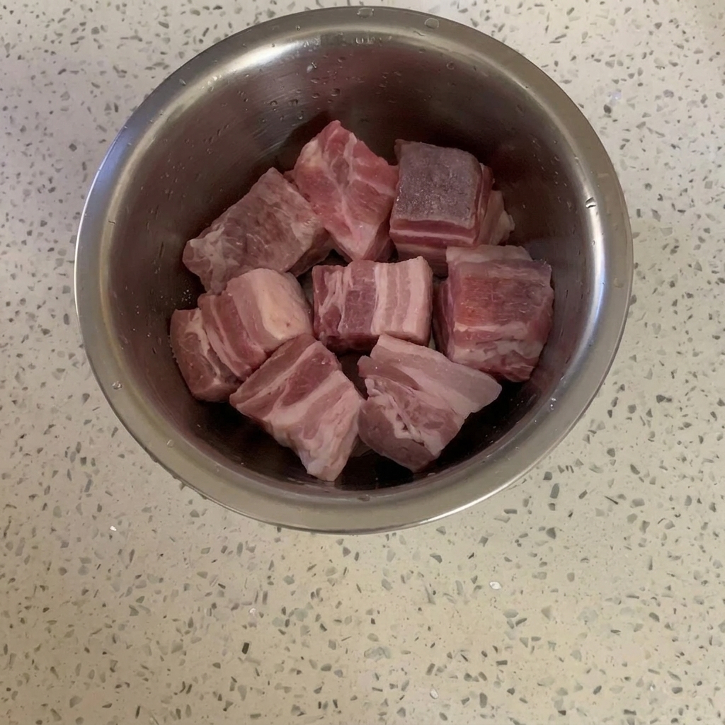 Cubetti di pancetta di maiale in una ciotola di metallo leggermente ricoperti di zucchero semolato.