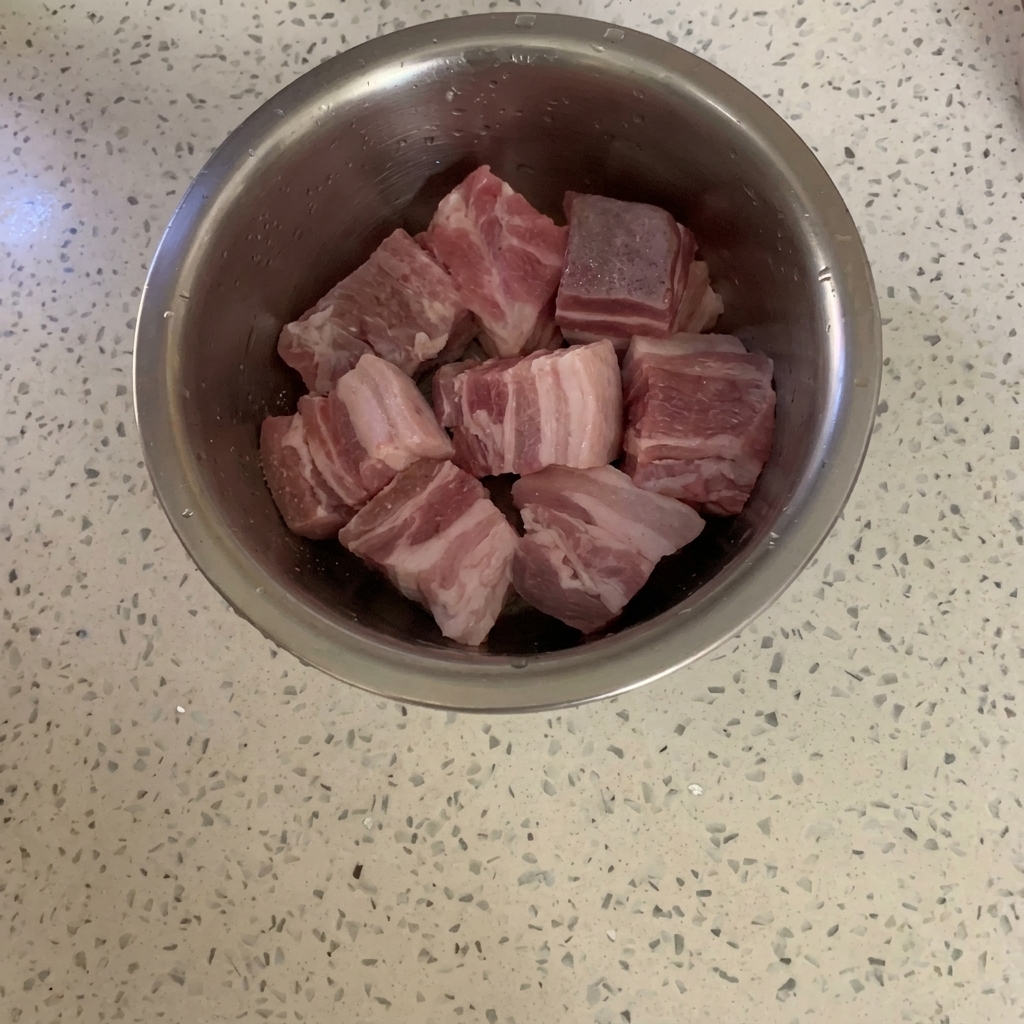 Ciotola di metallo con pancetta di maiale a cubetti spolverata di pepe in polvere.