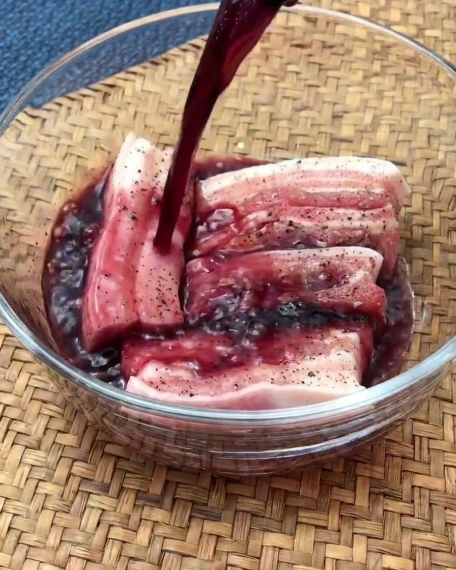 Fette di pancetta cruda a marinare in una ciotola di vetro riempita di vino rosso.