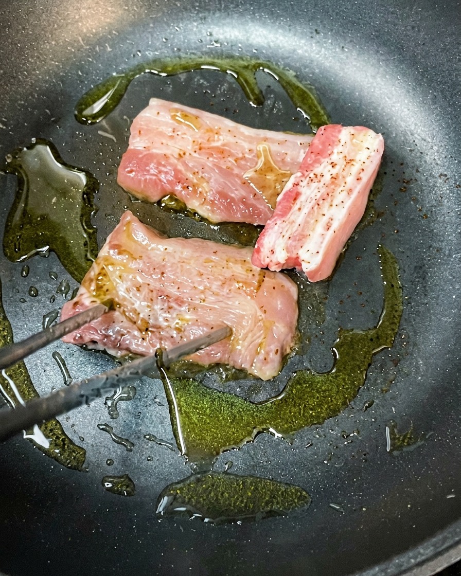 Fette di pancetta marinata che rosolano in una padella calda con olio doliva.