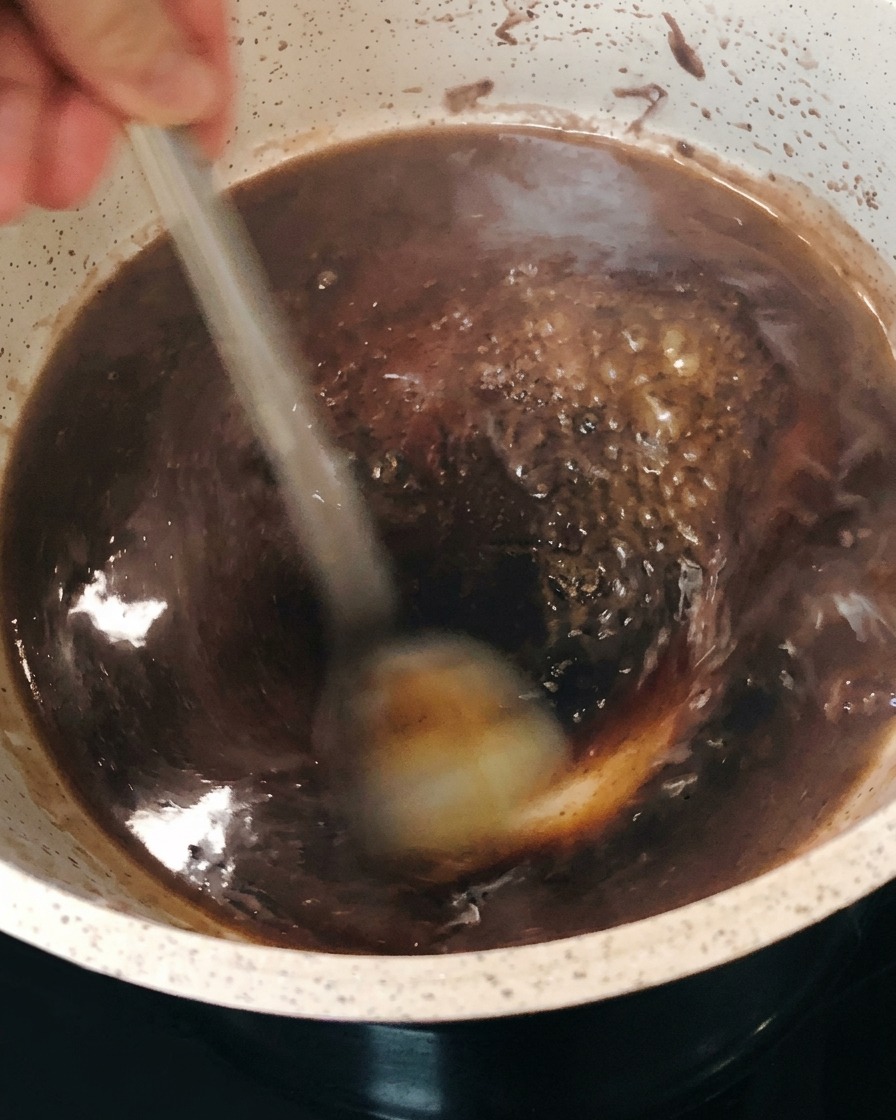 La riduzione di vino rosso scuro che bolle e si addensa nella pentola mentre viene mescolata.