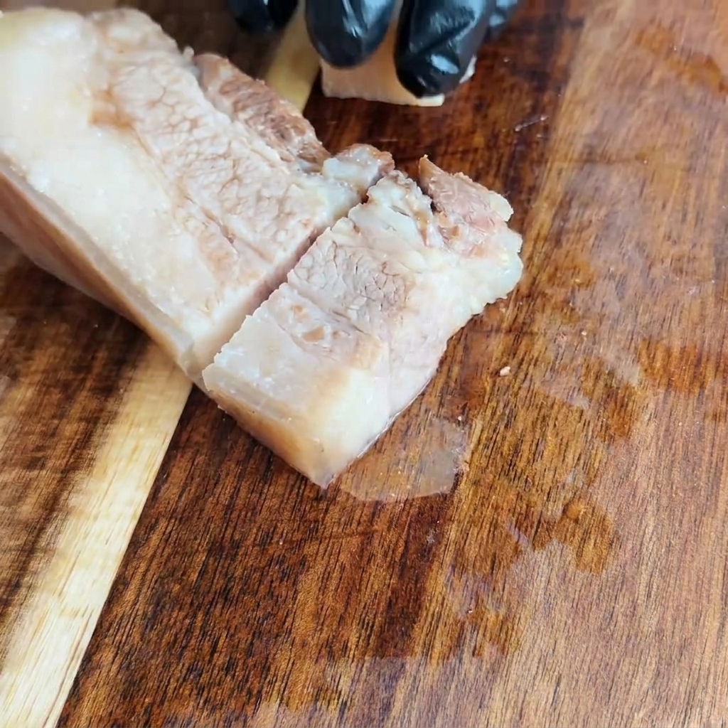 Pancia di maiale raffreddata tagliata in quadrati uniformi su un tagliere di legno.
