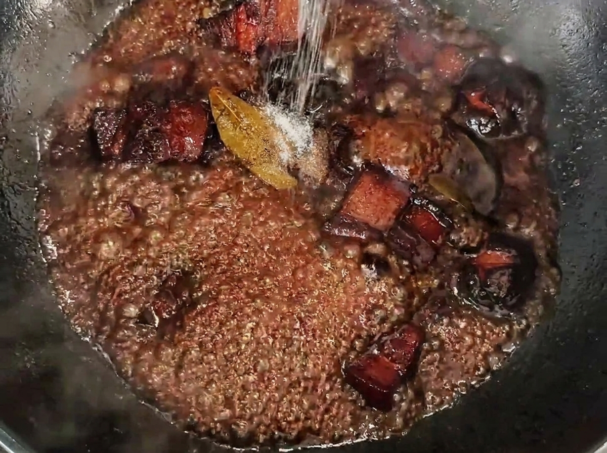 Sale cosparso sui cubetti di pancia di maiale che sobbollono in una salsa scura e ricca.