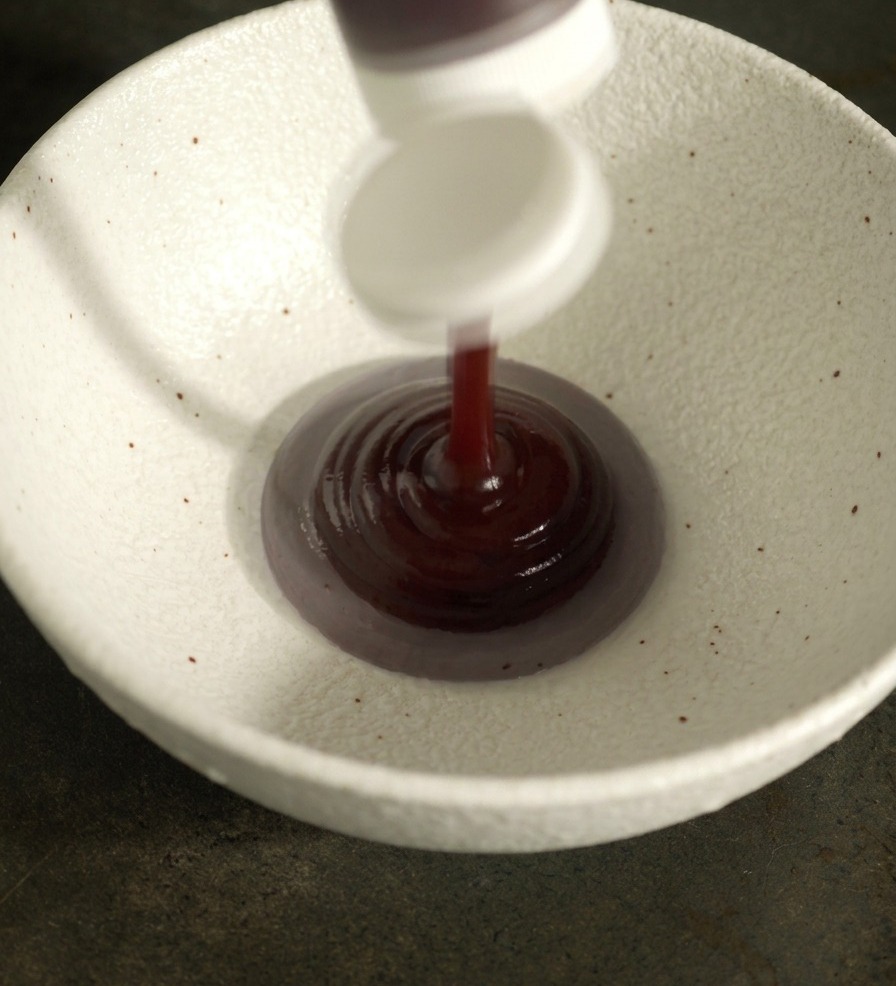 Salsa barbecue rosso scuro e altri condimenti liquidi versati in una ciotola di ceramica bianca.