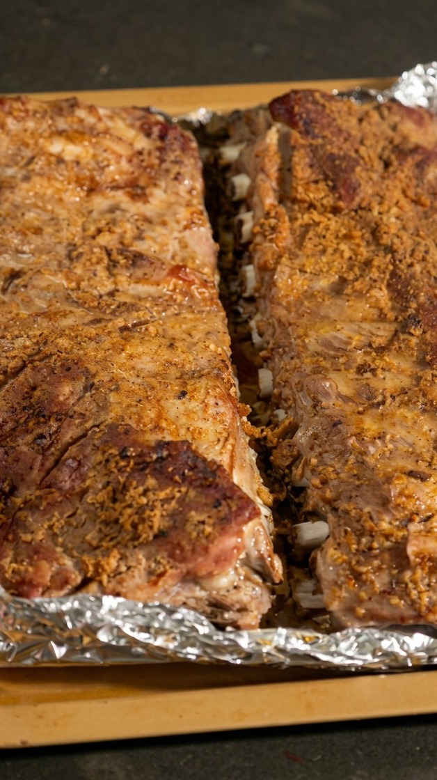 Due file di costine cotte su una teglia con lalluminio aperto per esporre la carne.