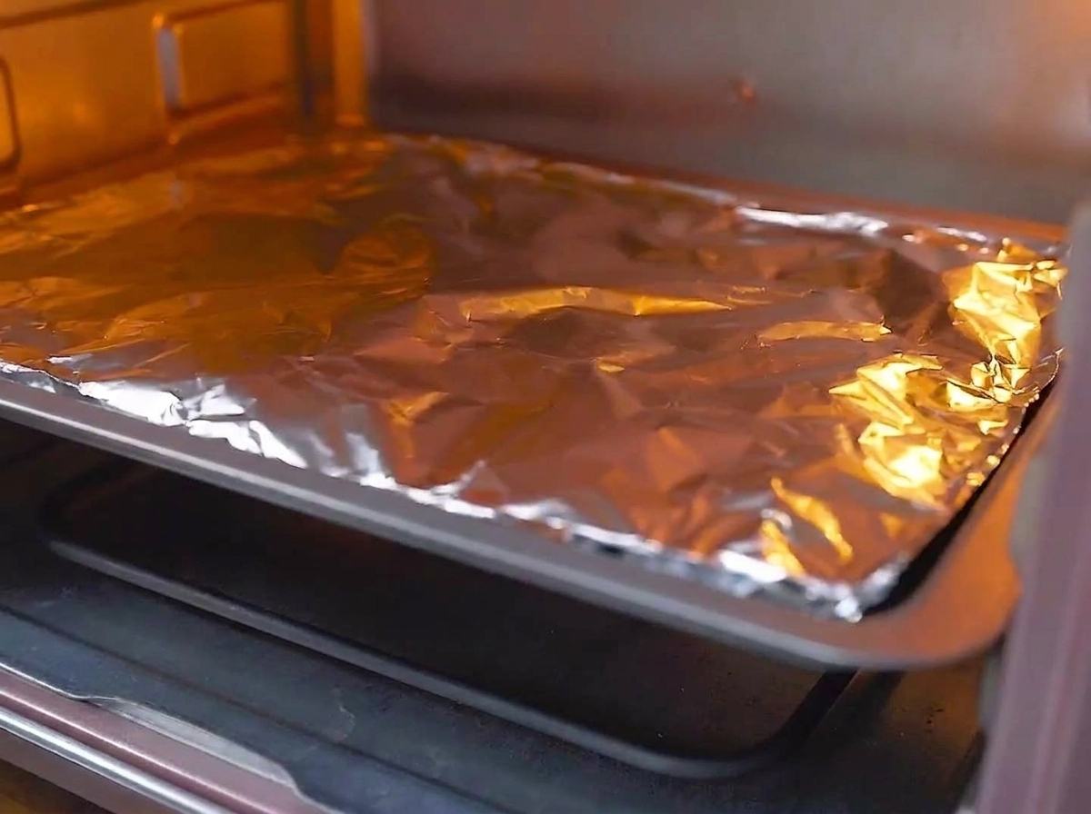 Una teglia coperta di alluminio inserita nel ripiano centrale di un forno preriscaldato e acceso.