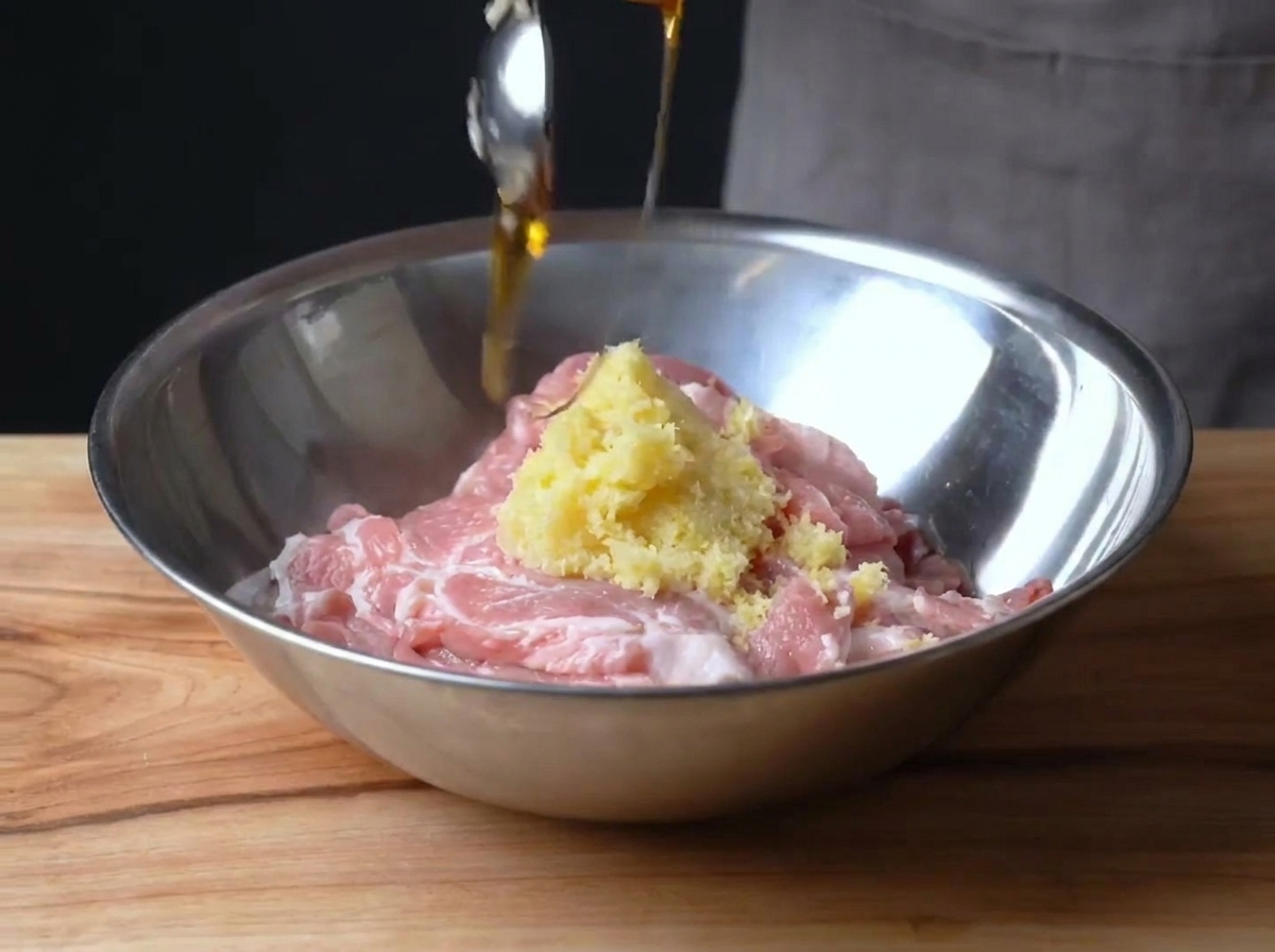 Maiale a fette in una ciotola di metallo mescolato con scorza di limone e sciroppo di mais.