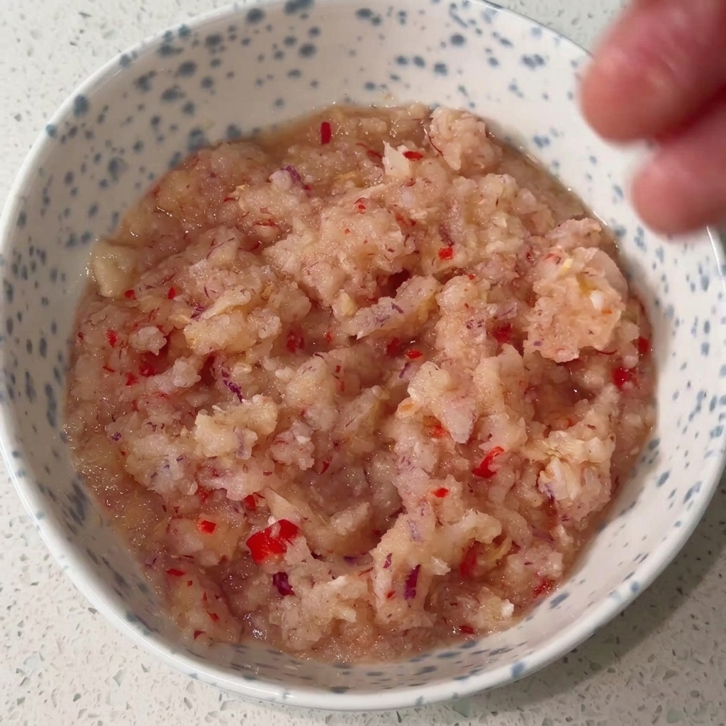 Una ciotola con base di cipolla e peperoncino mischiata con vari condimenti liquidi e in polvere.