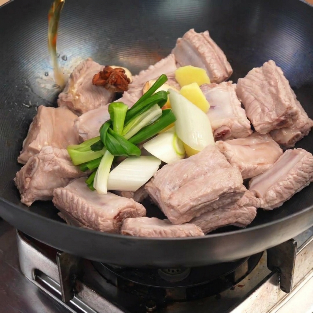 Costolette sbollentate in un wok con cipollotti annodati, zenzero e anice stellato mentre viene versato il liquido.