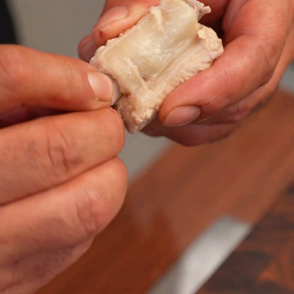 Mani che rimuovono con cura losso da un pezzo di costoletta cotta e lo farciscono con uno gnocco di riso bianco cilindrico.