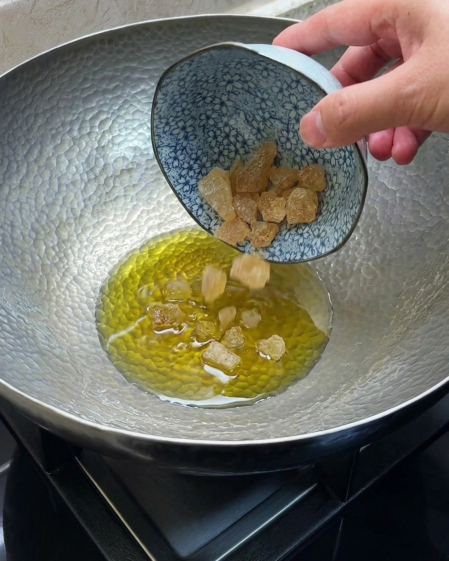 Zucchero di canna che si scioglie e caramella nellolio caldo allinterno di un wok di metallo.