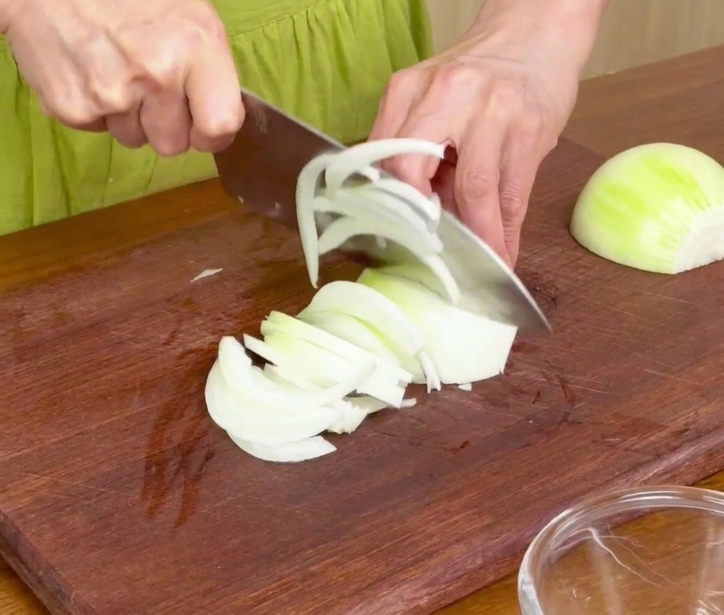 Affettare le cipolle bianche in strisce sottili su un tagliere di legno con un coltello da chef.
