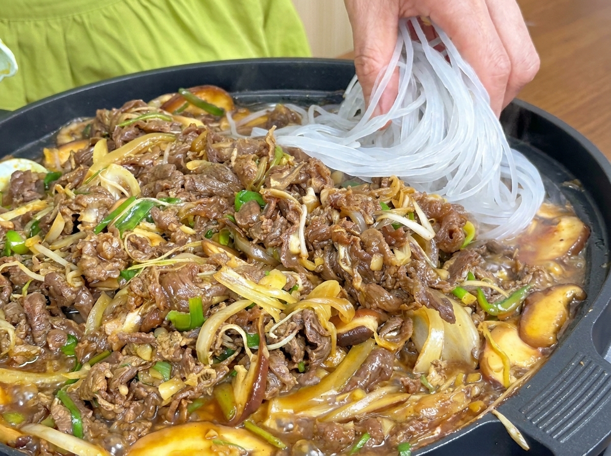 Vermicelli traslucidi che vengono aggiunti alla padella con manzo e verdure in cottura.
