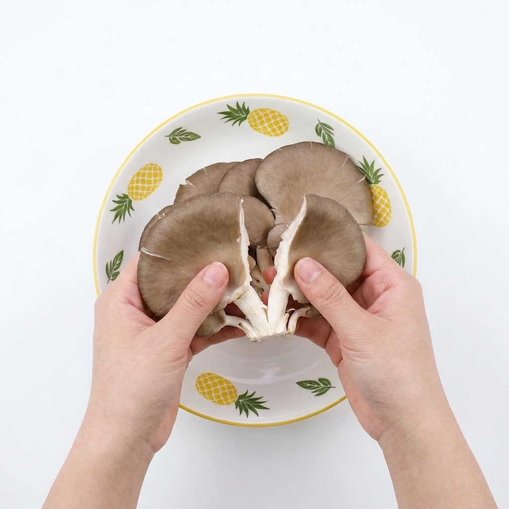 Mani che strappano funghi ostrica crudi in strisce più piccole sopra una ciotola decorata.