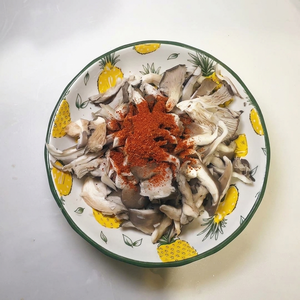 Un mucchio di peperoncino in polvere rosso sopra le strisce di funghi ostrica strizzate in una ciotola.