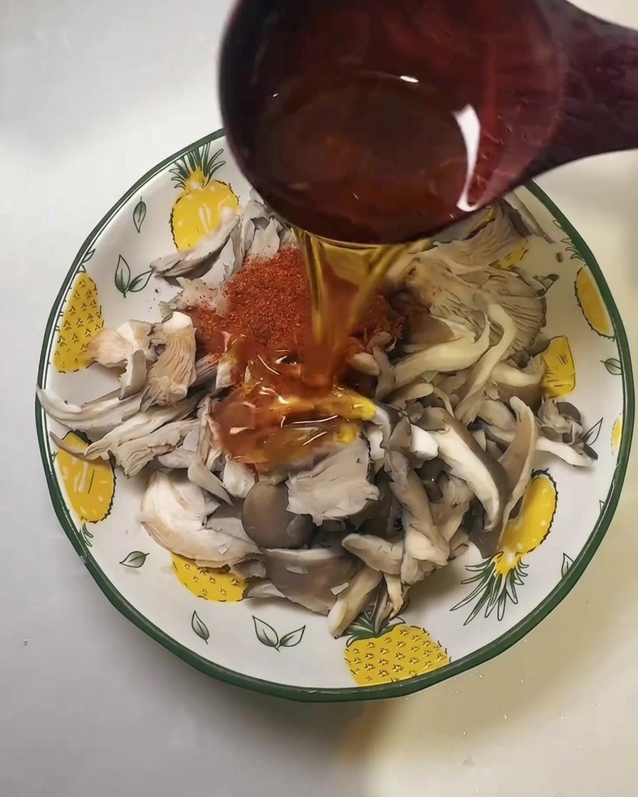 Olio da cucina versato da un mestolo di legno sopra il peperoncino in polvere e i funghi ostrica.