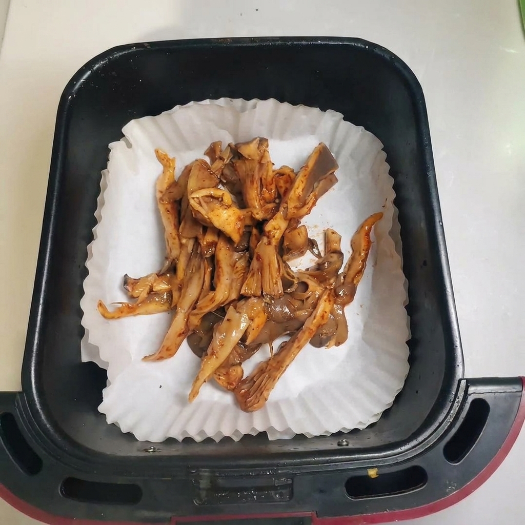Funghi conditi distribuiti in un cestello della friggitrice ad aria foderato con carta da forno.