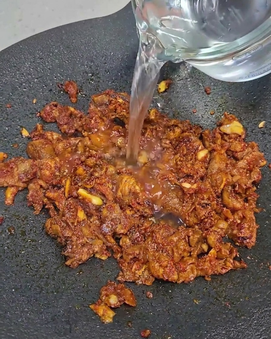 Fette di pancia di manzo che cuociono in una padella nera.