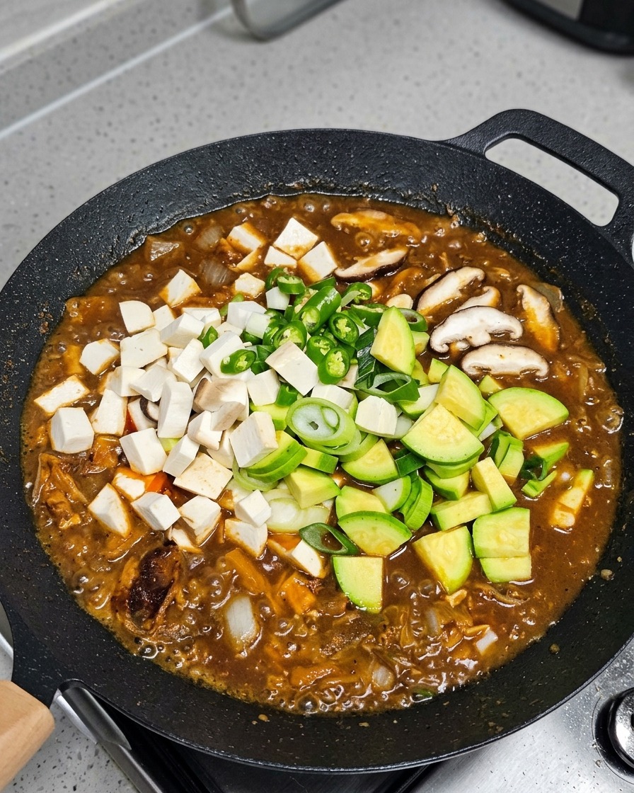 Verdure e tofu aggiunti allo stufato che sobbolle.