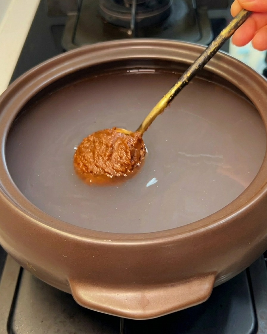 Un cucchiaio di pasta di soia marrone immerso nellacqua di un tegame di pietra.
