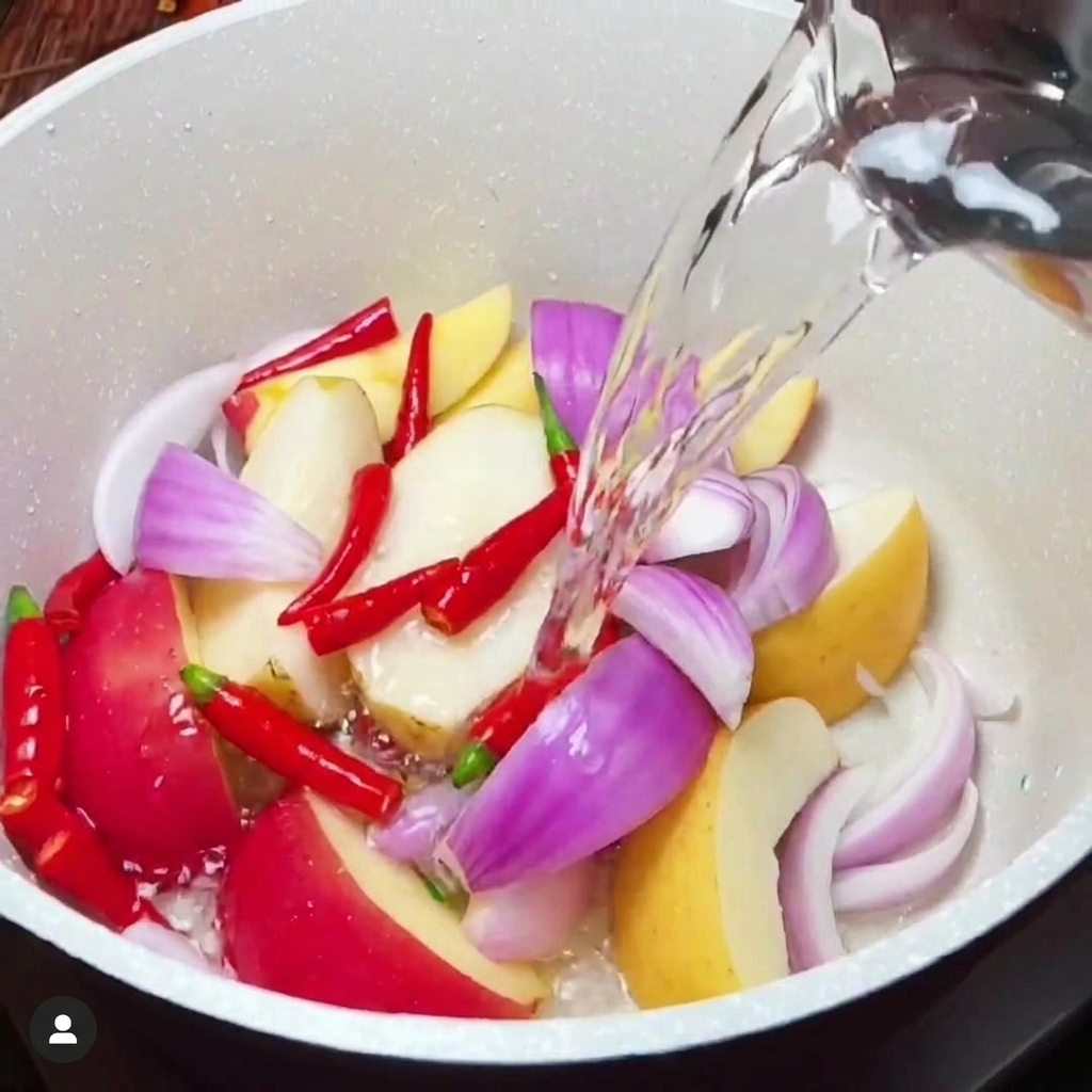 Condimenti liquidi versati in una pentola bianca contenente un mix di frutta e verdura tritata.