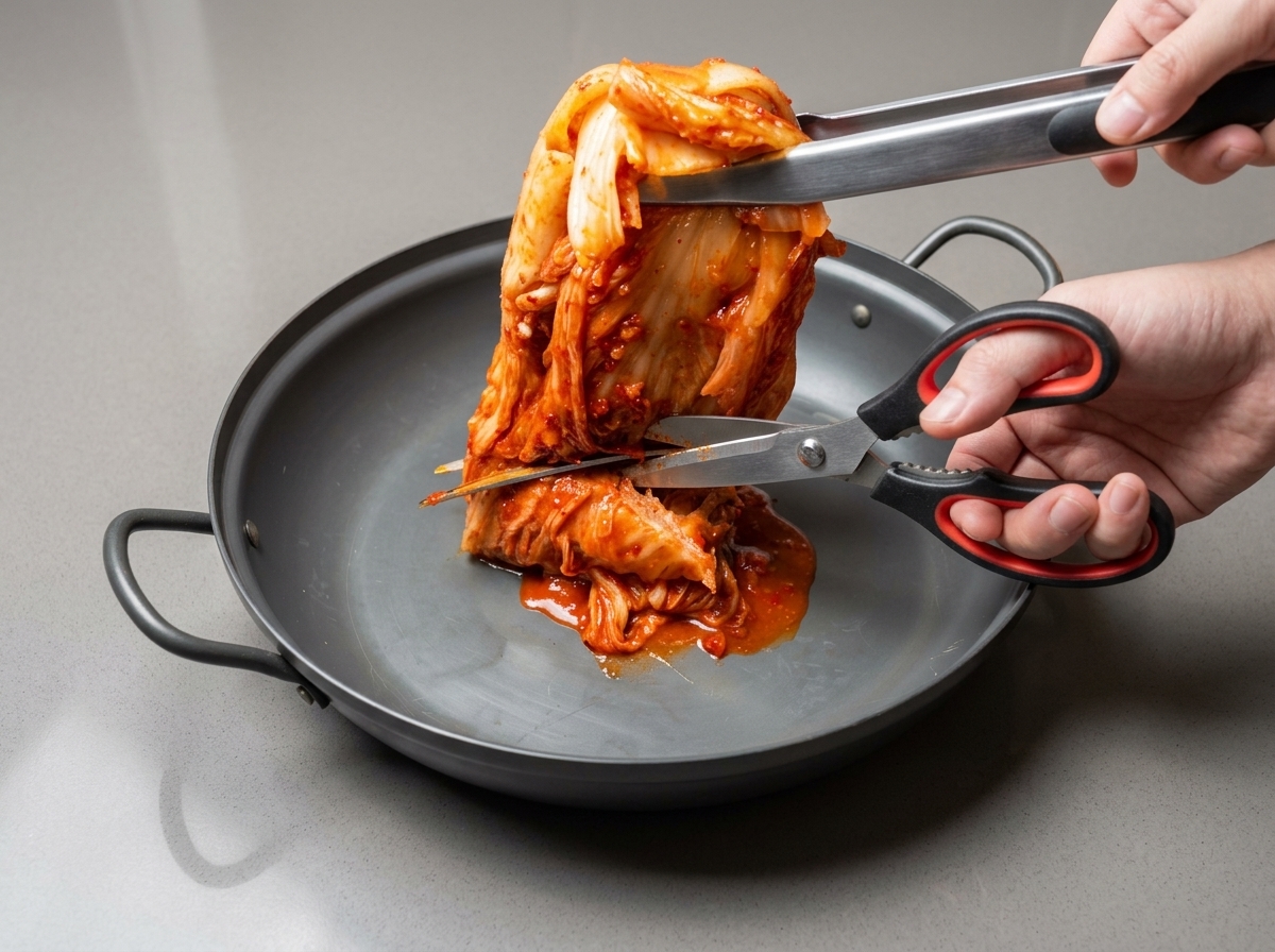 Forbici da cucina che tagliano il kimchi intero in pezzi più piccoli allinterno di una pentola capiente.