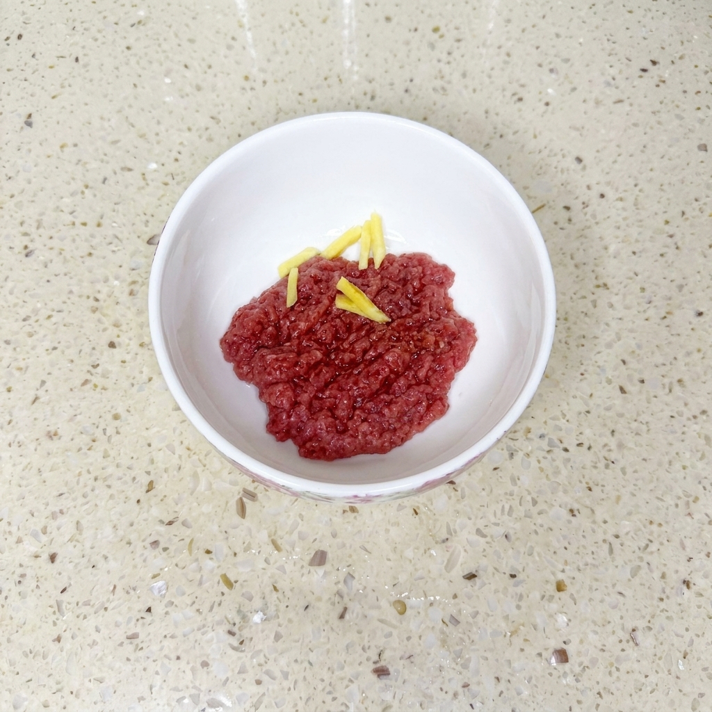 Manzo macinato in una ciotola bianca mescolato con salsa di soia, olio e amido di mais, guarnito con fettine di zenzero.