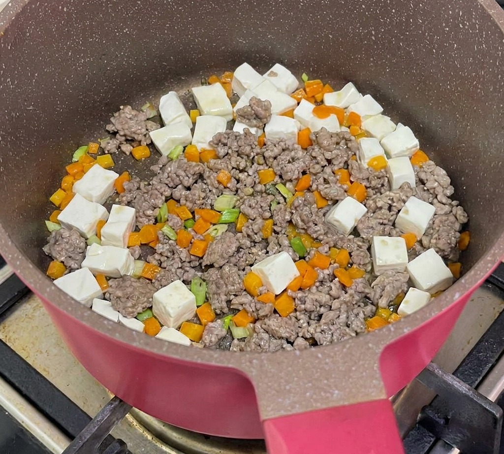 Acqua bollente versata nella padella contenente tofu, manzo e carote per la cottura.