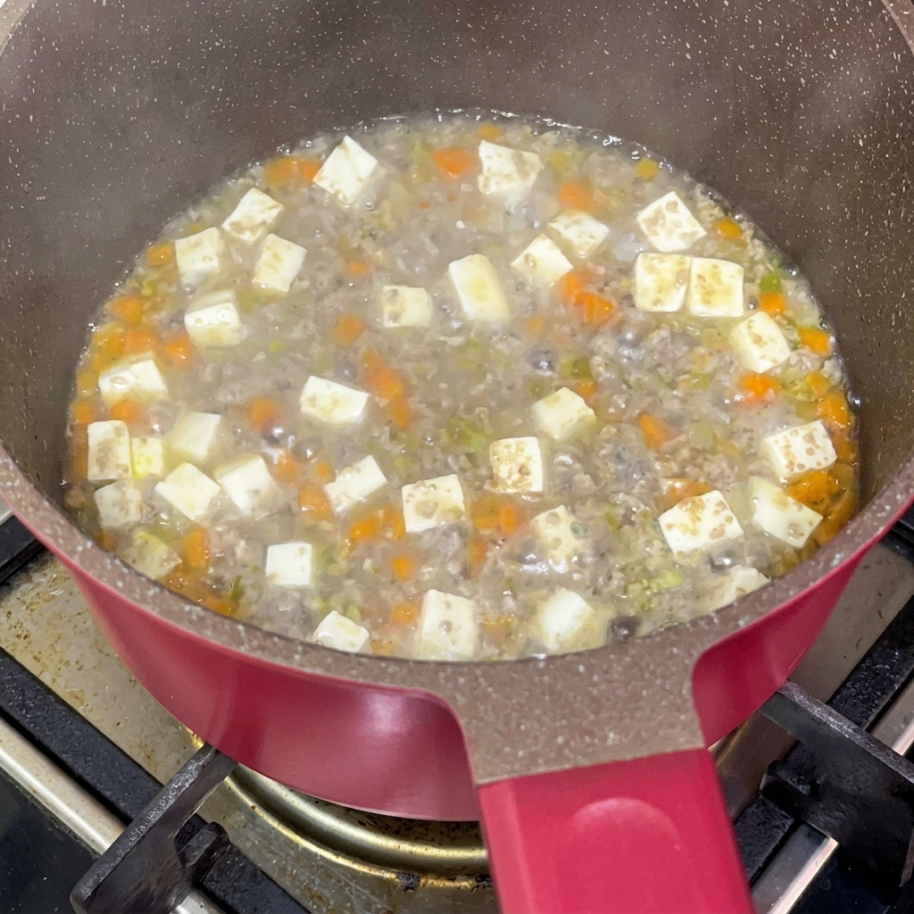 Salsa di soia aggiunta a un composto di manzo, tofu e carote che sobbolle in padella.