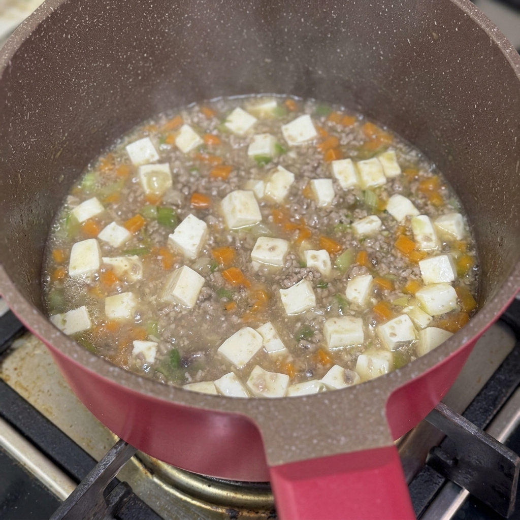 Cremina di amido di mais versata nella padella dello stufato di manzo e tofu che sobbolle.