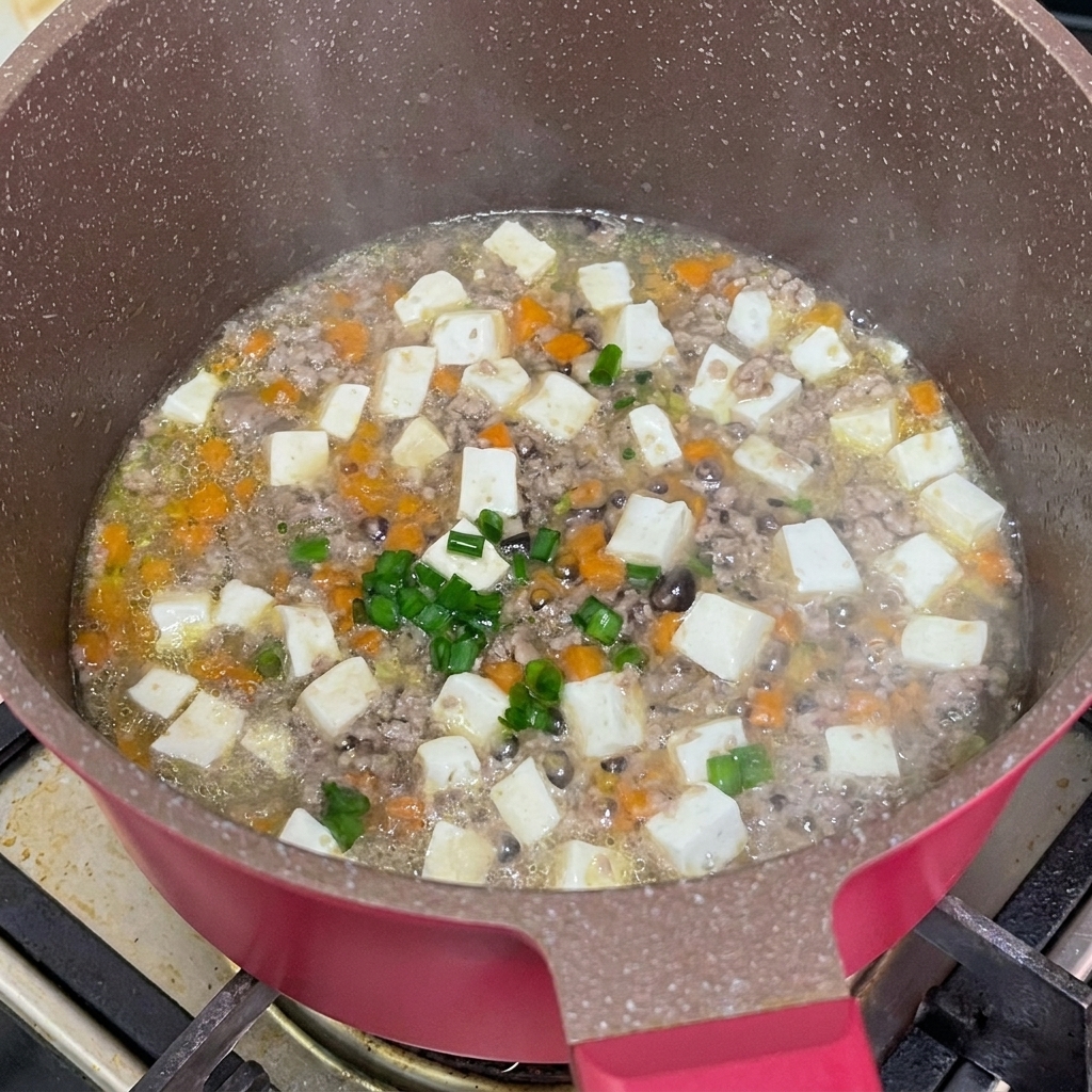 Scalogni freschi tritati cosparsi sopra lo stufato di manzo e tofu pronto in padella.